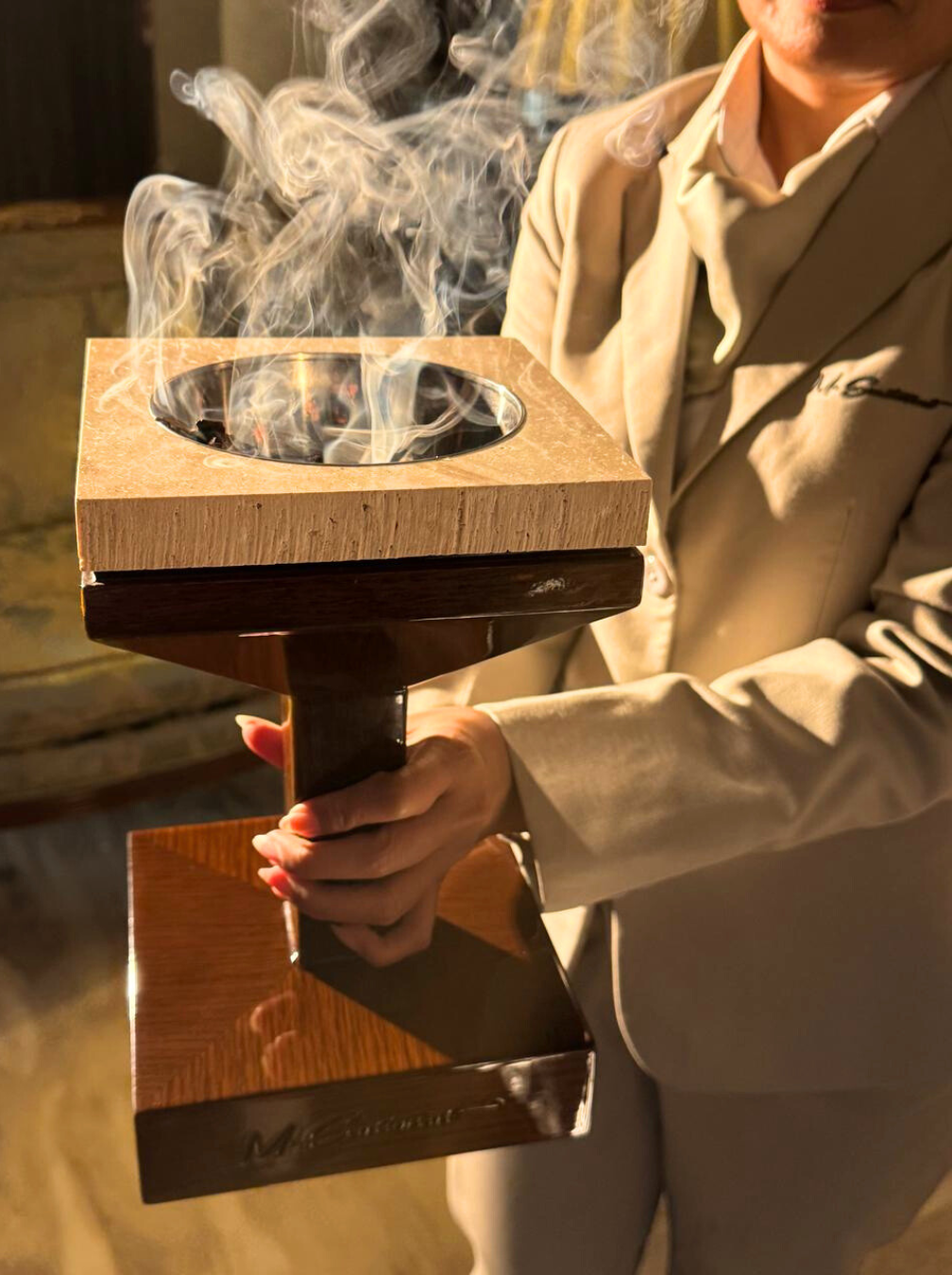 Person holding a wooden smoking device with smoke coming out, blurred background
